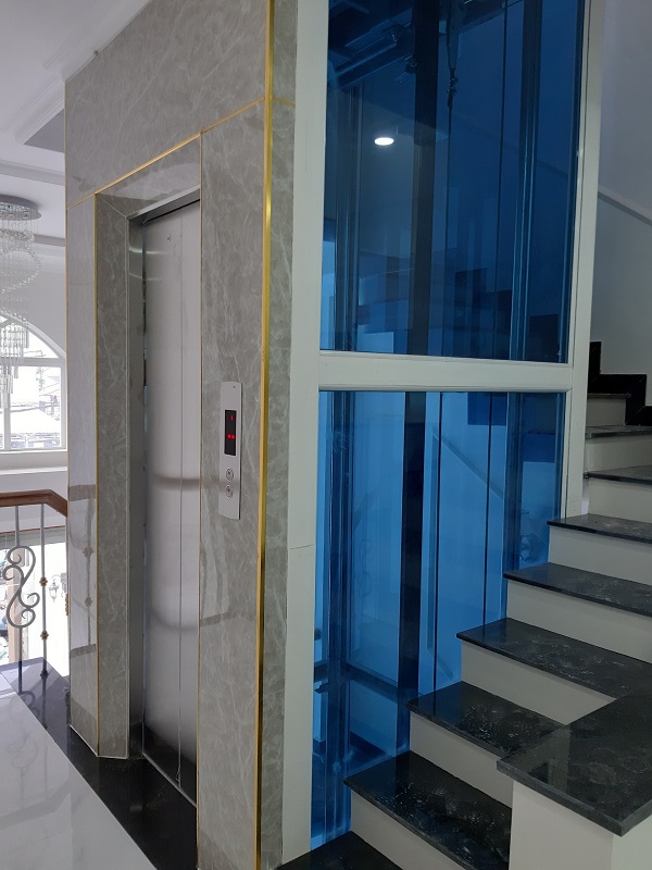 Thang máy giếng kính xanh lắp cạnh cầu thang đá trong nhà phố